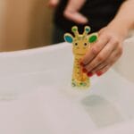 Dłoń trzymająca termometr w kształcie żyrafy w wanience niemowlaka