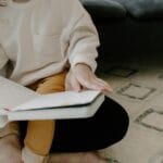 Małe dziecko siedzi na dywanie i ogląda kolorową książeczkę