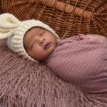 Śpiący noworodek w różowym otulaczu i czapce na miękkim kocyku