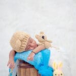 Śpiący noworodek z szydełkowym misiem i czapką w spokojnym otoczeniu