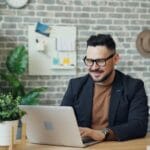 Uśmiechnięty mężczyzna pracuje na laptopie w nowoczesnym biurze