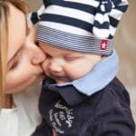 Mama całuje uśmiechnięte niemowlę na rękach podczas wspólnej podróży