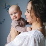 Mama trzyma uśmiechnięte niemowlę w przytulnym wnętrzu