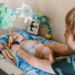 Niemowlę w łóżeczku sięga po kolorowe wiszące zabawki