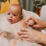 Niemowlę w pianie kąpielowej, mama delikatnie myje dziecko