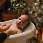 Noworodek delikatnie kąpany w wanience w przytulnej, ciepłej łazience