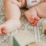 Stópki niemowlaka na dywanie wśród drewnianych klocków