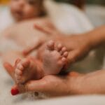 Stopy niemowlęcia w kąpieli trzymane delikatnie przez dorosłe dłonie