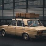 Beżowy sedan z bagażem na dachu jedzie autostradą obok miasta