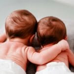 Bliźnięta w pieluszkach leżące obok siebie na łóżku