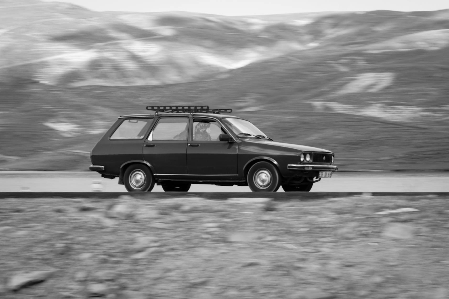 Klasyczne kombi jedzie górską drogą na czarno-białej fotografii