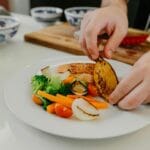 Szef kuchni układa na talerzu grillowanego łososia z warzywami