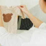 Kobieta ogląda beżowy sweterek niemowlęcy z misiem jako pomysł na prezent