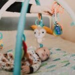Niemowlę bawiące się na macie z wiszącymi, kolorowymi zabawkami