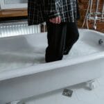 Osoba w zalanej wodą wannie w łazience w ubraniu