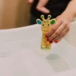 Ręka trzyma termometr w kształcie żyrafy w wanience niemowlęcej