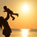 Mama unosi niemowlę na tle zachodu słońca nad morzem