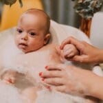 Niemowlę w kąpieli wśród piany, mama delikatnie myje dziecko