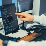 Programista piszący kod na laptopie i monitorze w biurze