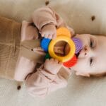 Niemowlę leżące na miękkim podłożu gryzie kolorowy gryzak