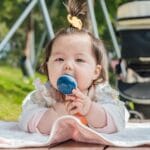 Niemowlę na kocu na dworze trzyma zabawkę obok wózka