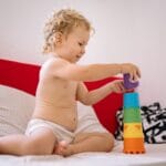 Niemowlę budujące wieżę z kolorowych klocków na sofie